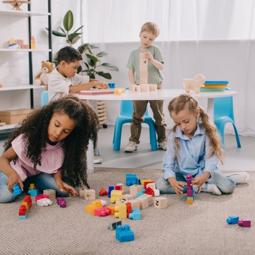 focused multiracial preschoolers playing with wooden blocks in classroom